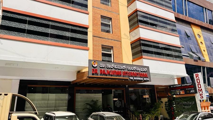 Exterior front view of Hotel Dr Rajkumar International with visible signage, parked vehicles and entrance.
