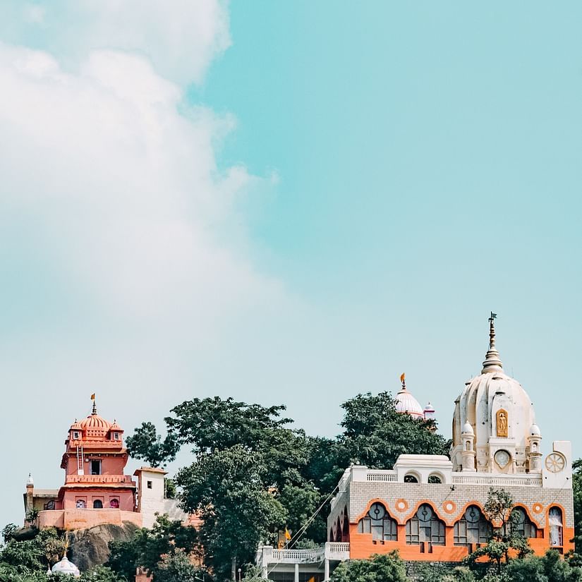 A hilltop temple with domes and spires, brightly colored against a cloudy sky.