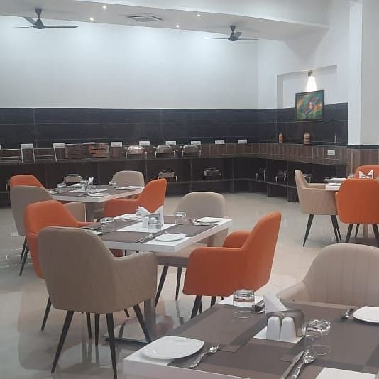 A restaurant shows tables set for dining with dark chairs and lighting - Kankidham Lords Inn