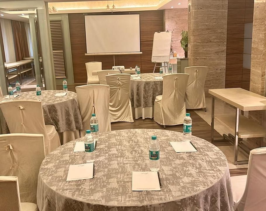  Round banquet tables with silver covers and chairs, ample seating area, projector and wooden flooring at Mirage Hotel, Mumbai.