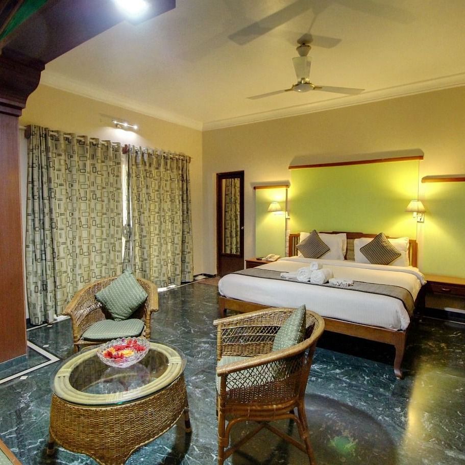 A well-lit room at Damanganga Valley Resorts in Silvassa featuring a plush bed and a sitting space in front of it including a coffee table and couches