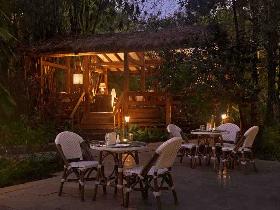 Outdoor dining area with elegant chairs and warm lighting in a garden at Amanvana Spa Resort, Coorg.
