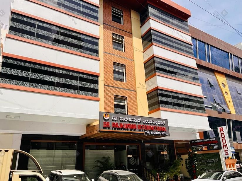 Exterior front view of Hotel Dr Rajkumar International with visible signage, parked vehicles and entrance.