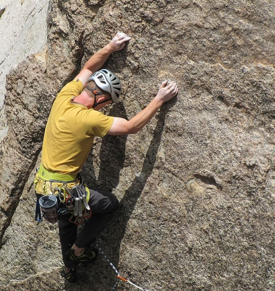 An image of a man wearing helmet climbing rock who has several metal locks tied to his waist 