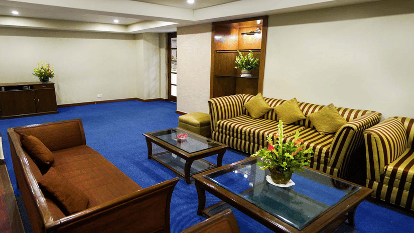 A room with blue carpeting, striped sofas, wooden armchairs, and glass-topped coffee tables | HHI Varanasi