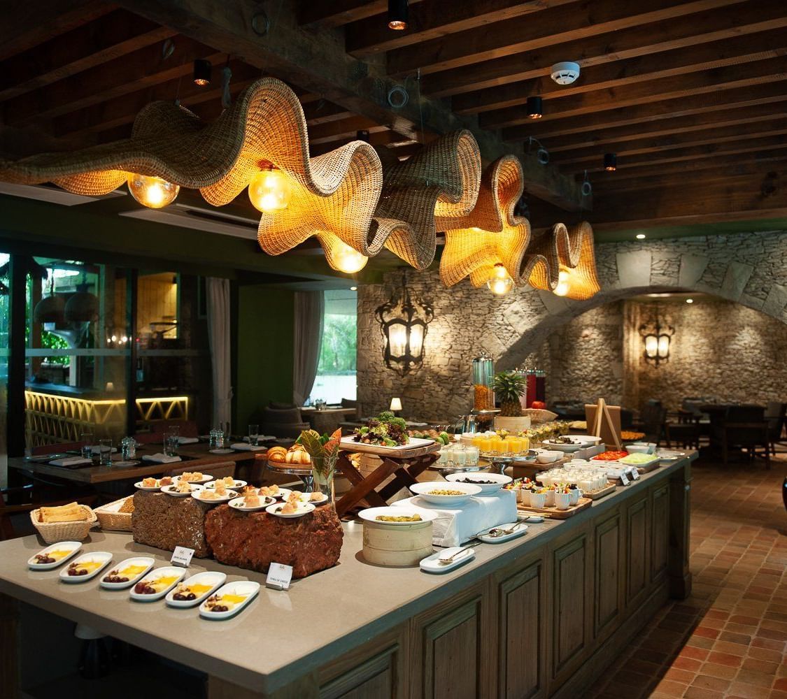 A lavish breakfast buffet spread at the Mila Restaurant at The Evren, Vagator, featuring a variety of dishes on display under the woven light fixtures.