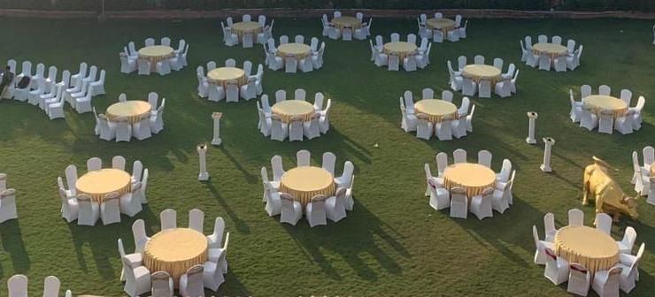 Outdoor banquet arrangement with round tables and chairs set on the lawn for a reception at Ilara Hotels & Spa, OMR, Chennai