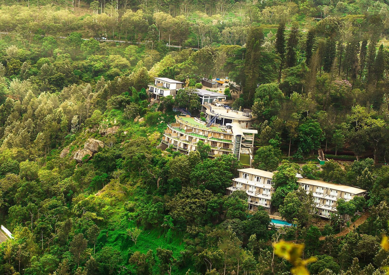 Drone shot of the hotel surrounded by mountains with sun light hitting the lush greenery - Great Trails Yercaud by GRT Hotels