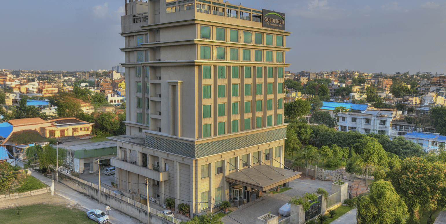 Wide aerial shot showing the multi-story exterior building of Goldfinch Bengaluru surrounded by greenery.