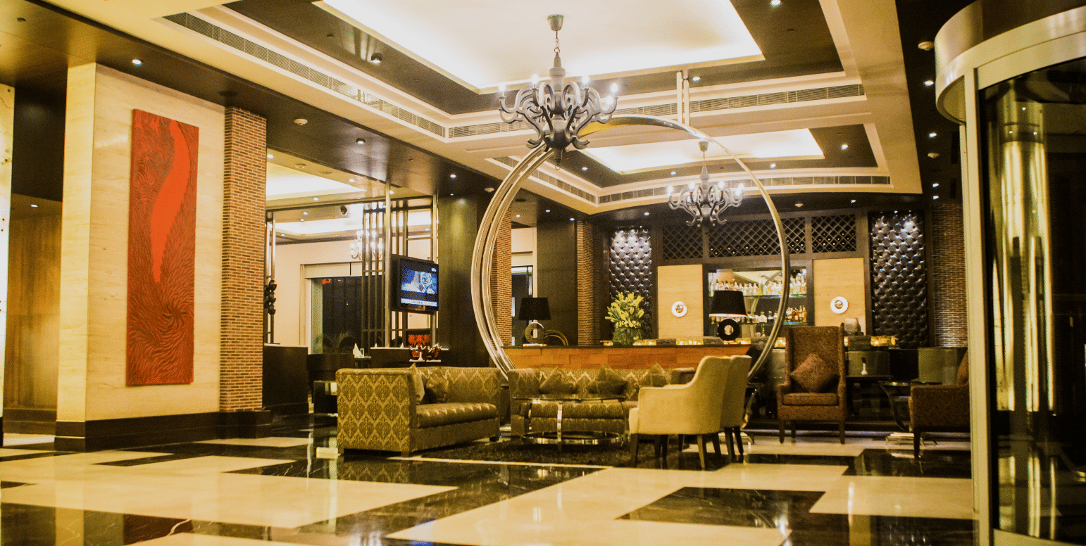 Hotel foyer at Goldfinch Bengaluru with reflective flooring, comfortable sofas, decorative wall panel, and entry doors.