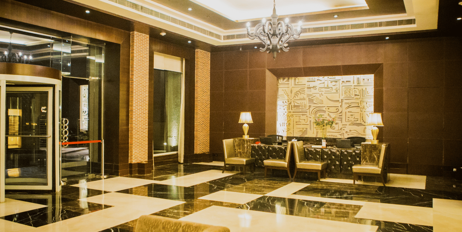 Hotel lobby area at Goldfinch Bengaluru displaying glossy tiled floors, plush couches, wall decor, and glass doors.