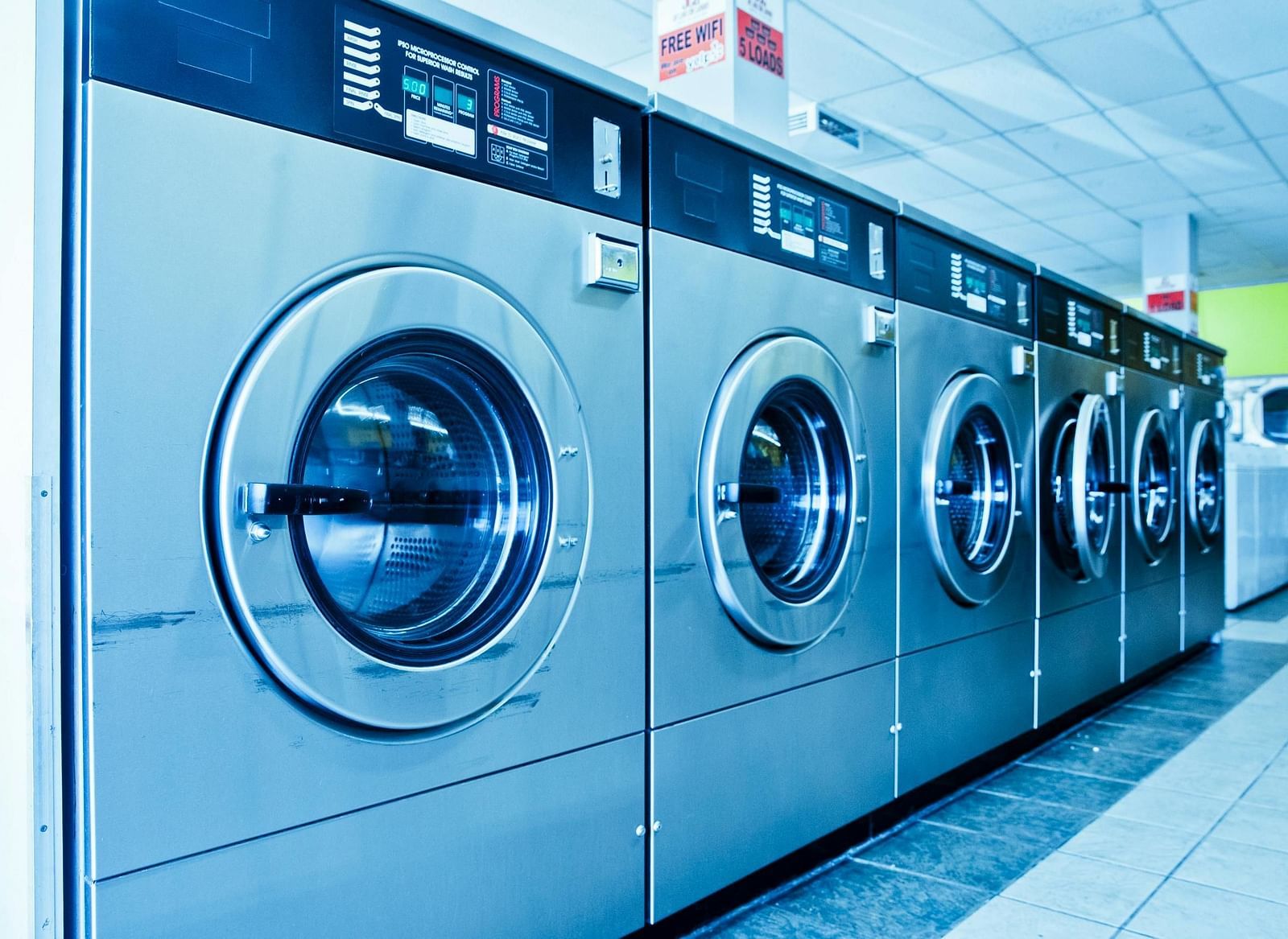 A row of silver coloured, front load washing machines lined up.