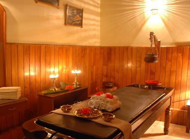 Warmly lit spa treatment room with a massage table and various wellness products - BluSalzz Collection - Tranquil Resort, Wayanad