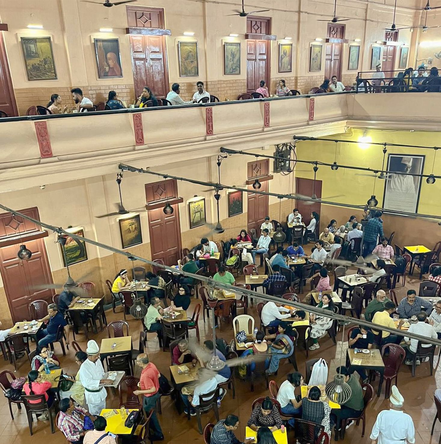 A restaurant space with packed people and waiters handing over the food to different tables.