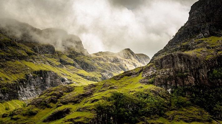 a valley in between two mountains with dark clouds in the background 