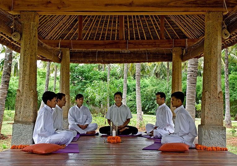 People sitting on cushions under a wooden gazebo, outdoor setting, group activity - Shreyas Retreat