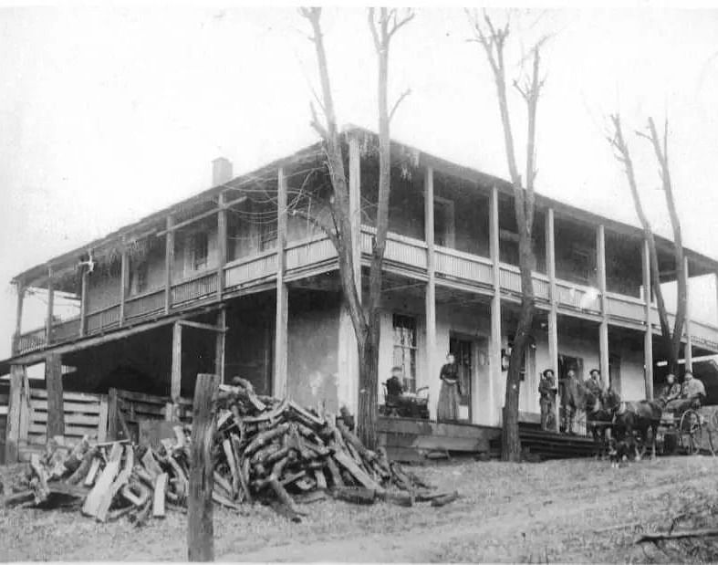 A black and white image of a building with trees surrounding it being logged - The Groveland Hotel.