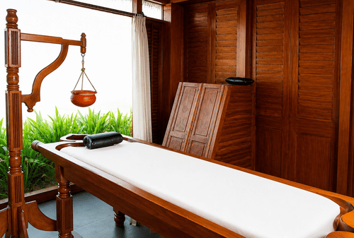 Spa massage table setup with warm wooden furnishings and traditional decor at Chariot Beach Resort, designed for a relaxing treatment.