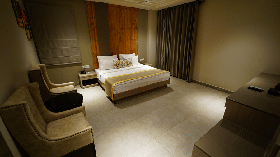Wide angle view of a room at Five Elements Hotel with a king bed, lounge chair, dark curtains, and warm golden ambient lighting.