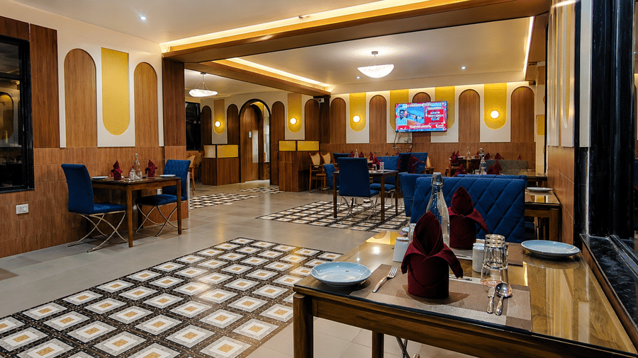 Elegant restaurant interior featuring upholstered lounge chairs, wooden tables, warm cove lighting, and patterned flooring at Kali Mirch Restaurant, Lords Riverside Resort, Muduba.