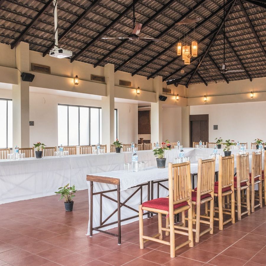 The airy and open dining hall at Forest Escapes Koyna features long tables and chairs, with natural light streaming in.