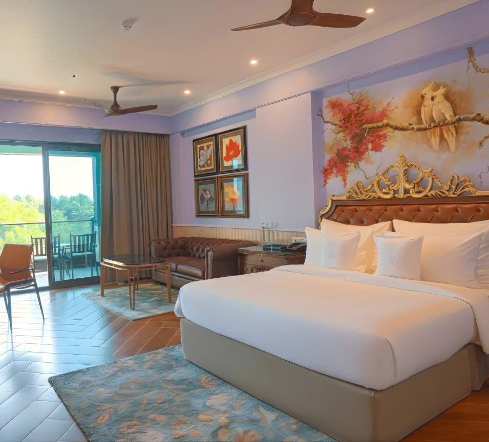 A spacious guest room with twin beds, wooden flooring, ceiling fan, cosy seating by the window, framed artwork and large windows offering greenery views at MAYFAIR Bay Resort, Paradeep.