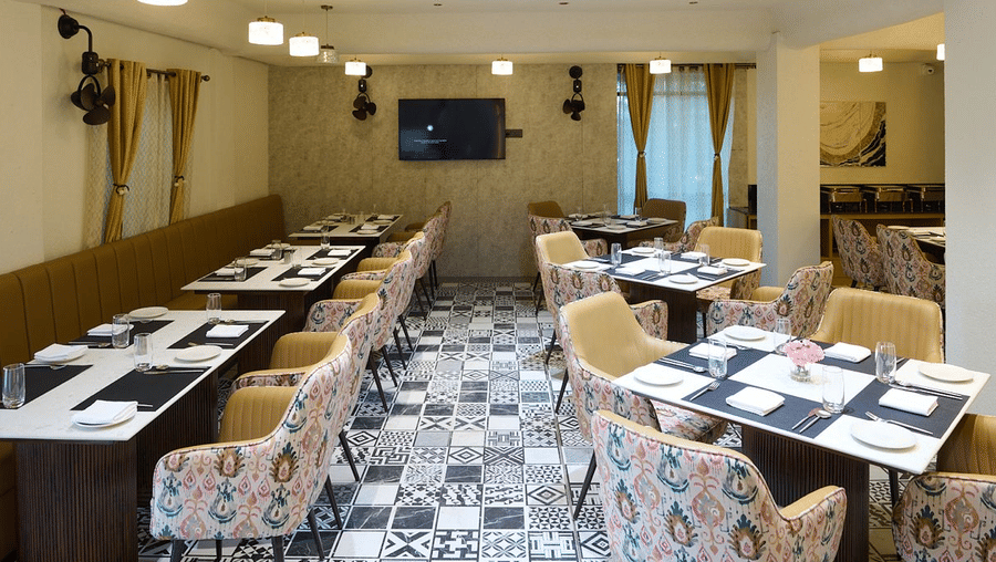 An indoor restaurant dining area with set tables, patterned chairs, and a central TV screen | Voyage Eastin Suites