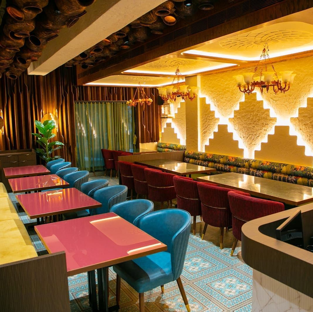 A dining area showing blue and red seating, a brick wall, unique wooden chandeliers, and decorative wall plates.