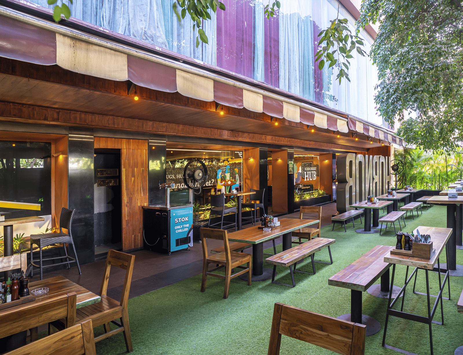 An outdoor seating area with tables, chairs and a long building wall decorated with signs at Infiniti Hotel, Indore.