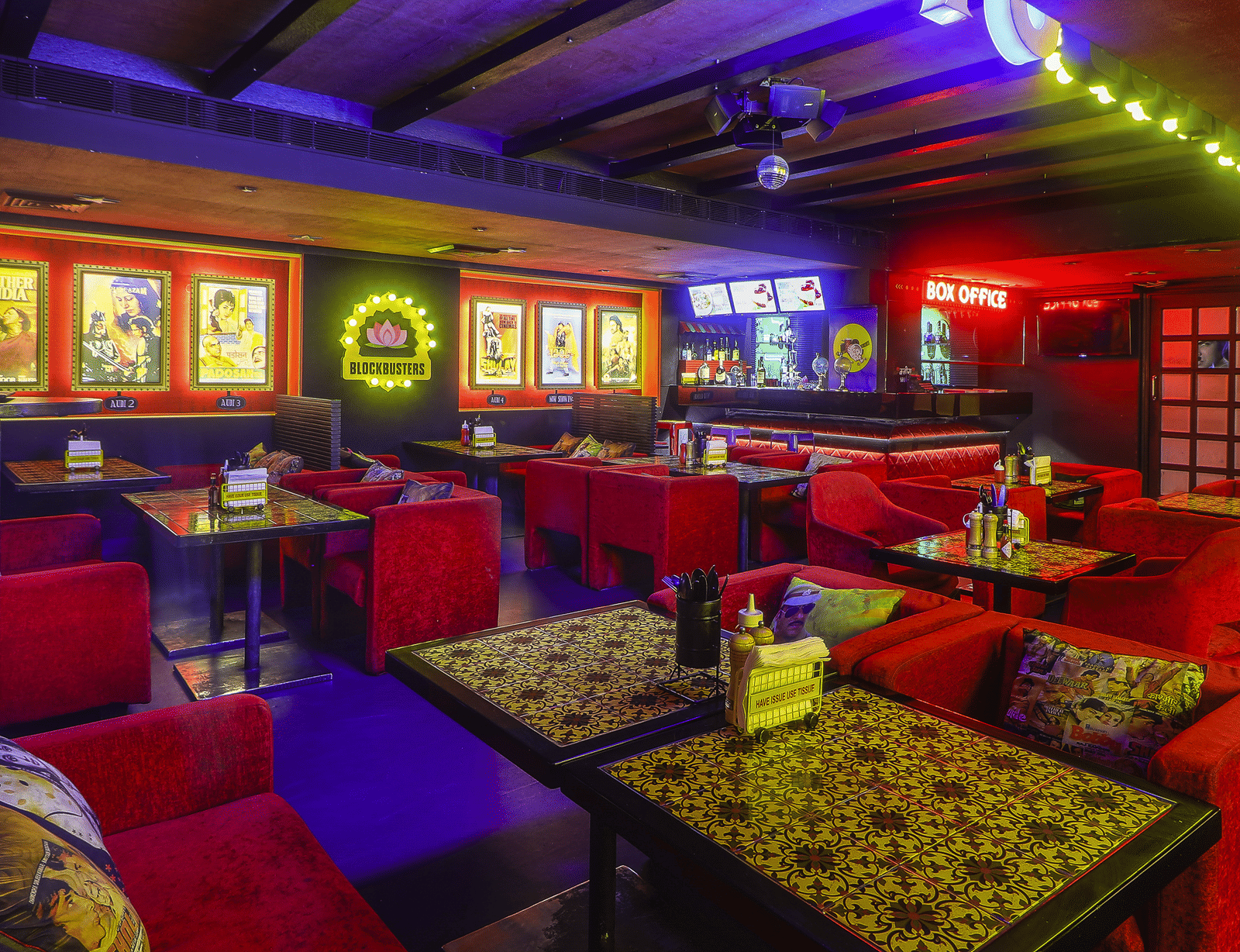 Rows of red sofas and dining tables with framed Bollywood posters and neon lights at Infiniti Hotel, Indore.