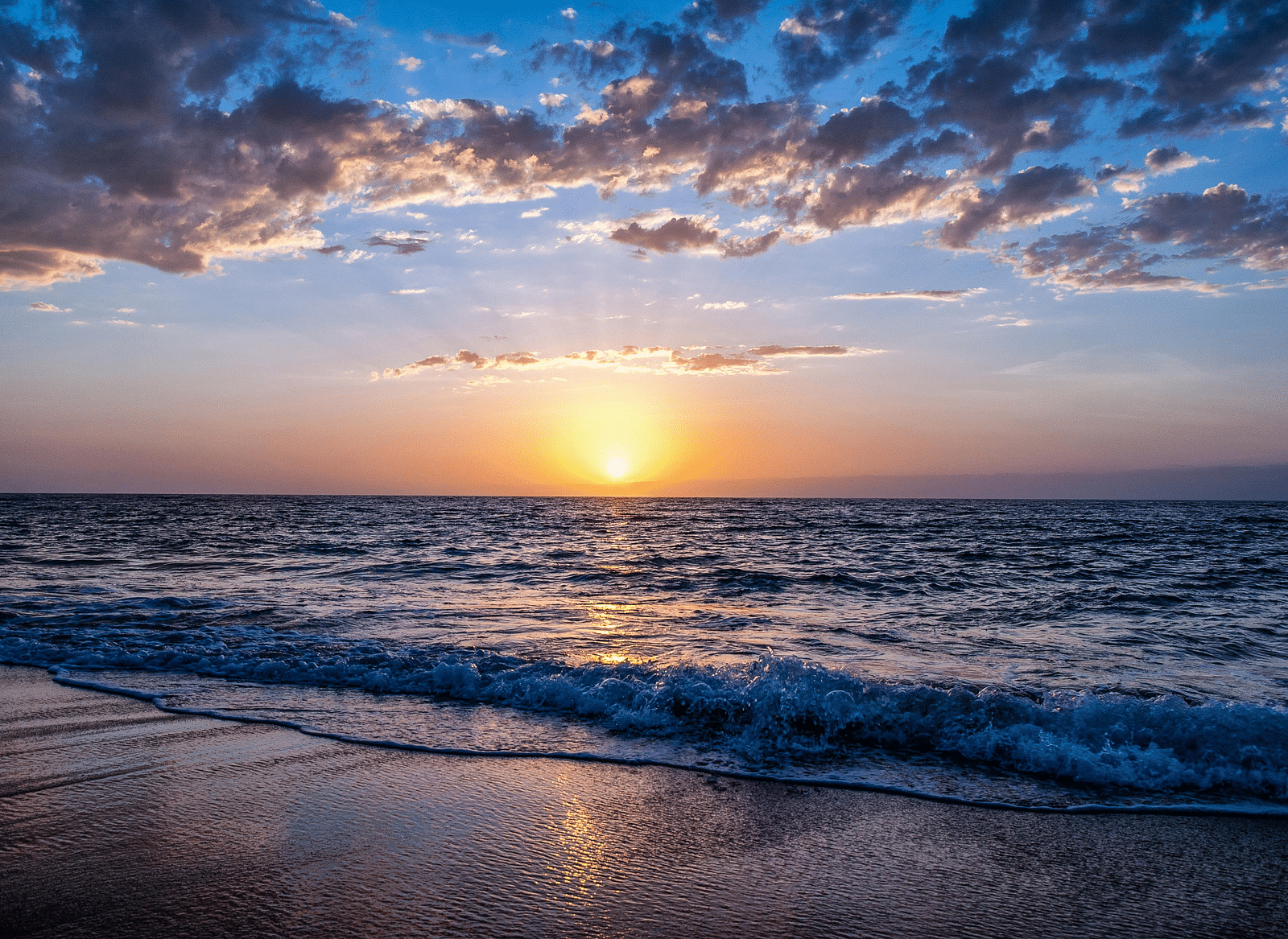A beachfront view of the sunrise with clouds scattered across the sky.