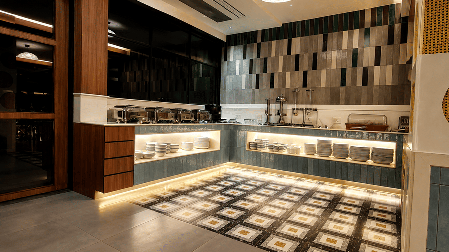 Illuminated buffet station with a marble countertop, tiled accent wall, and wooden storage units at Kali Mirch Restaurant, Lords Riverside Resort, Muduba.