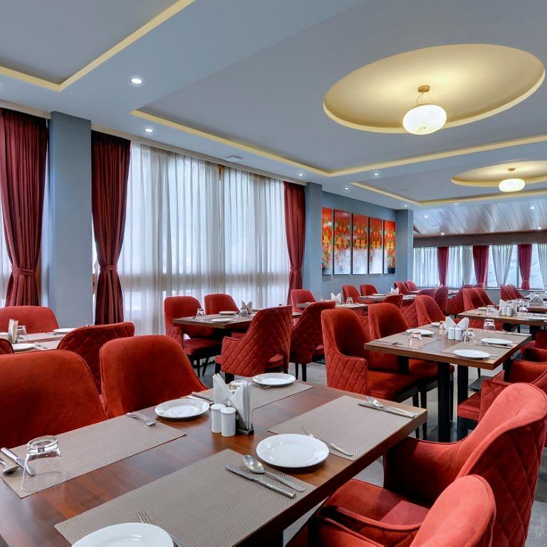 Shot of  the restaurant at the hotel with red chair and tables with plates arranged  | Yashshree Lachung