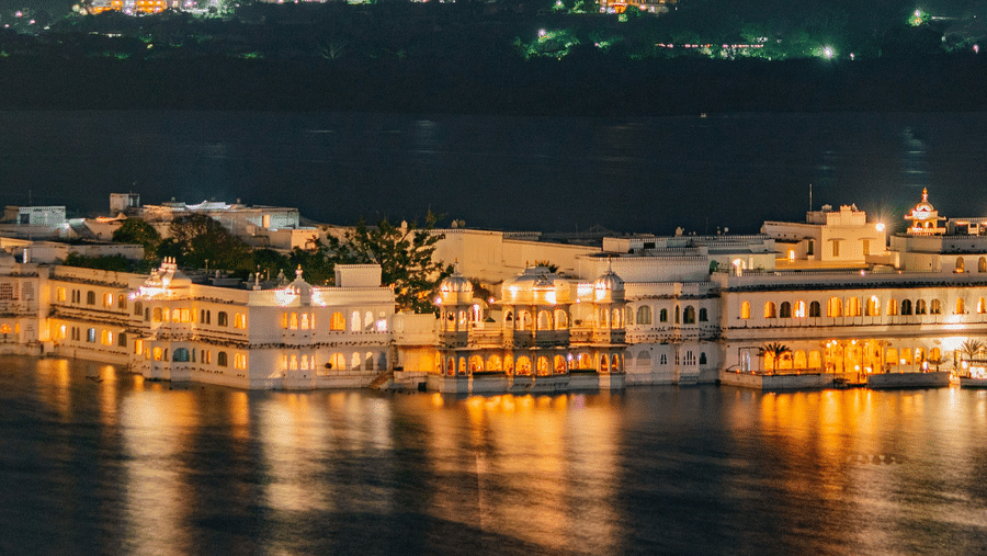 An aerial view of a palace in middle of a water body illuminated by bright yellow lights