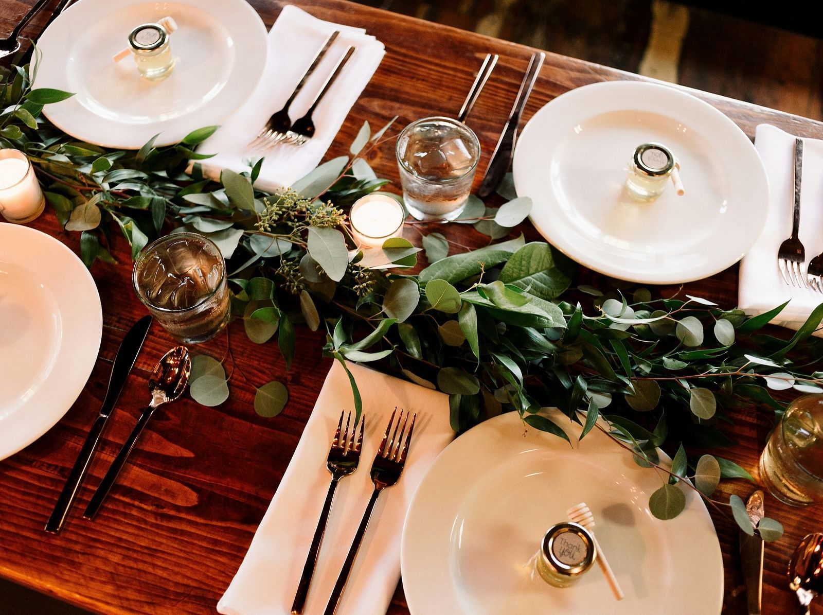 A wooden table with plates and  forks placed on either side of a decorative plant set up