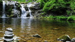 A shot at the Jalagamparai Waterfalls with stone cairn on the water body, and  the waterfall amidst the canopy.