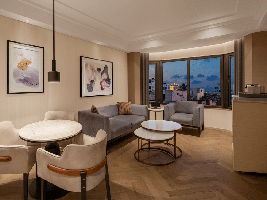 Elegant living area of a spacious suite room at The Residency Chennai, showcasing a stylish sofa set, framed artwork on the walls, and a round table.