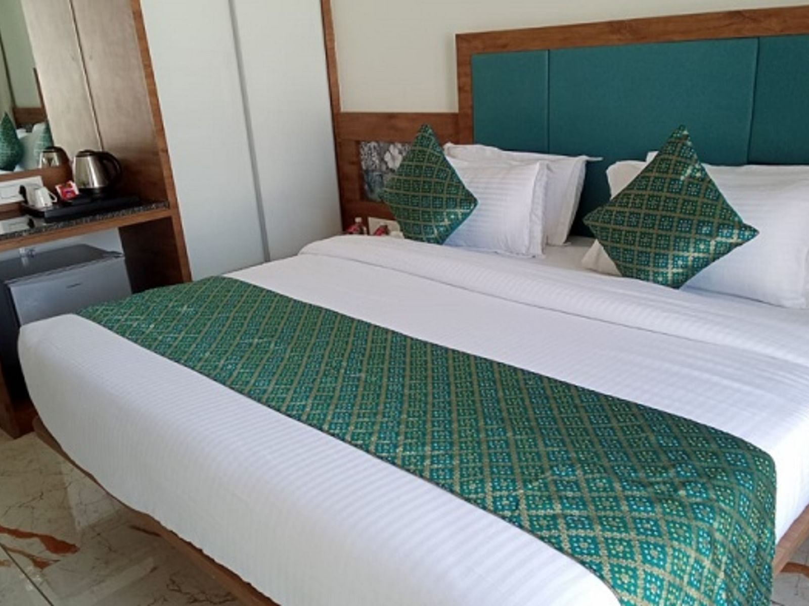 A room with a large bed which is neatly made with bedsheet, pillows and bedside tables at Angel Lords Eco Inn Amreli.