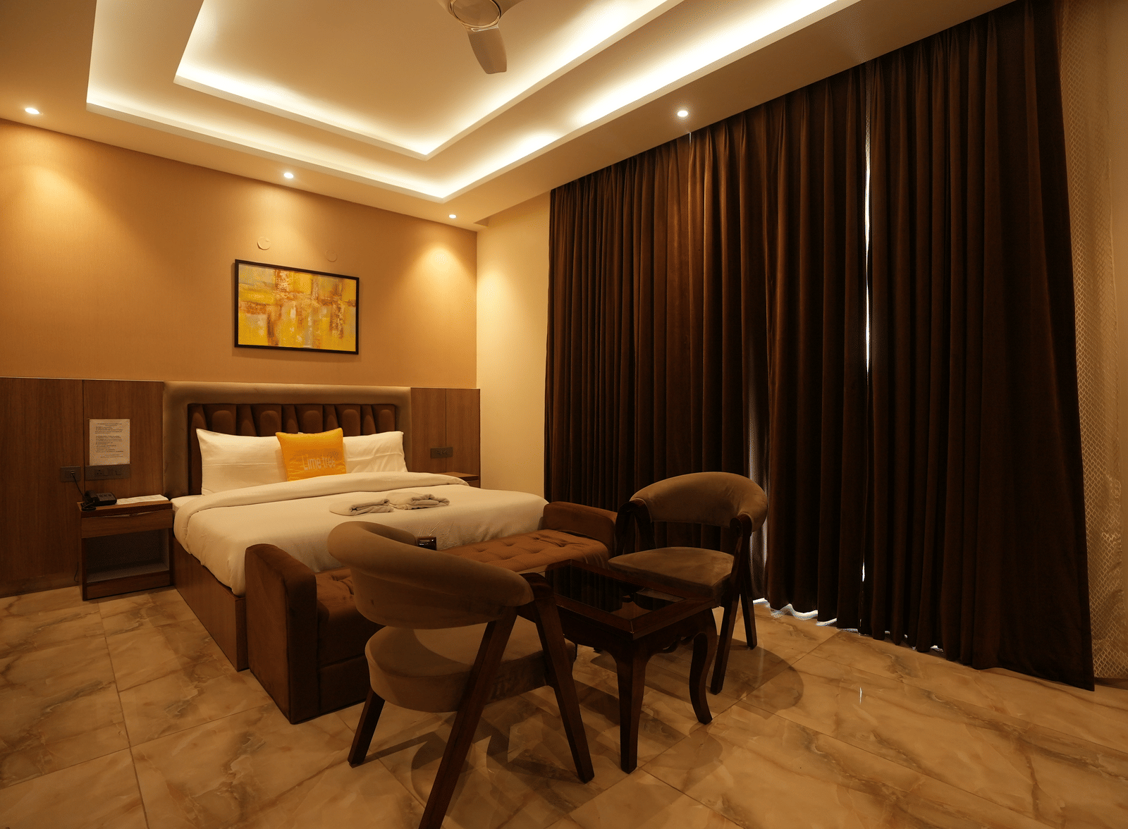 Room with a king size bed, seating area, ceiling-to-floor window, and soft lighting at Lime Tree Hotel & Banquet, Greater Noida.