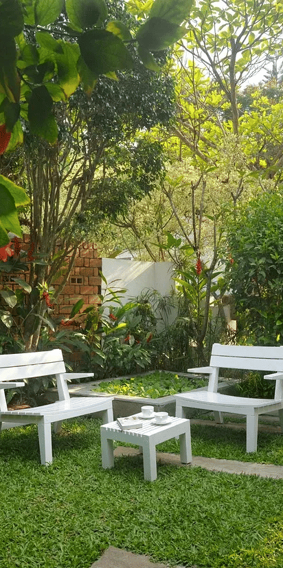 White garden seating set on a green lawn surrounded by trees and plants at Amanvana Spa Resort in Coorg.