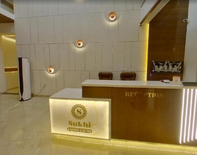Reception area with a wooden desk featuring an illuminated logo, set against a backdrop of textured walls and ambient lighting.- Sukhi - A Luxury Stay Inn, Chikkamagaluru