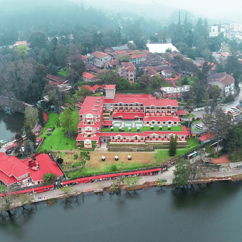 Aerial view of The Carlton Kodaikanal with red-roofed resort buildings, lush greenery, and a serene lake surrounding the property.