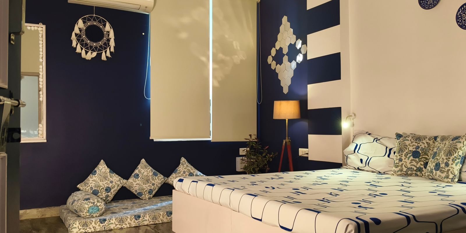 A bedroom with a double bed, patterned bedding, cushions, chairs and a decorative wall backdrop at Jaypore360 Homestay - Best Rooms in Jaipur.