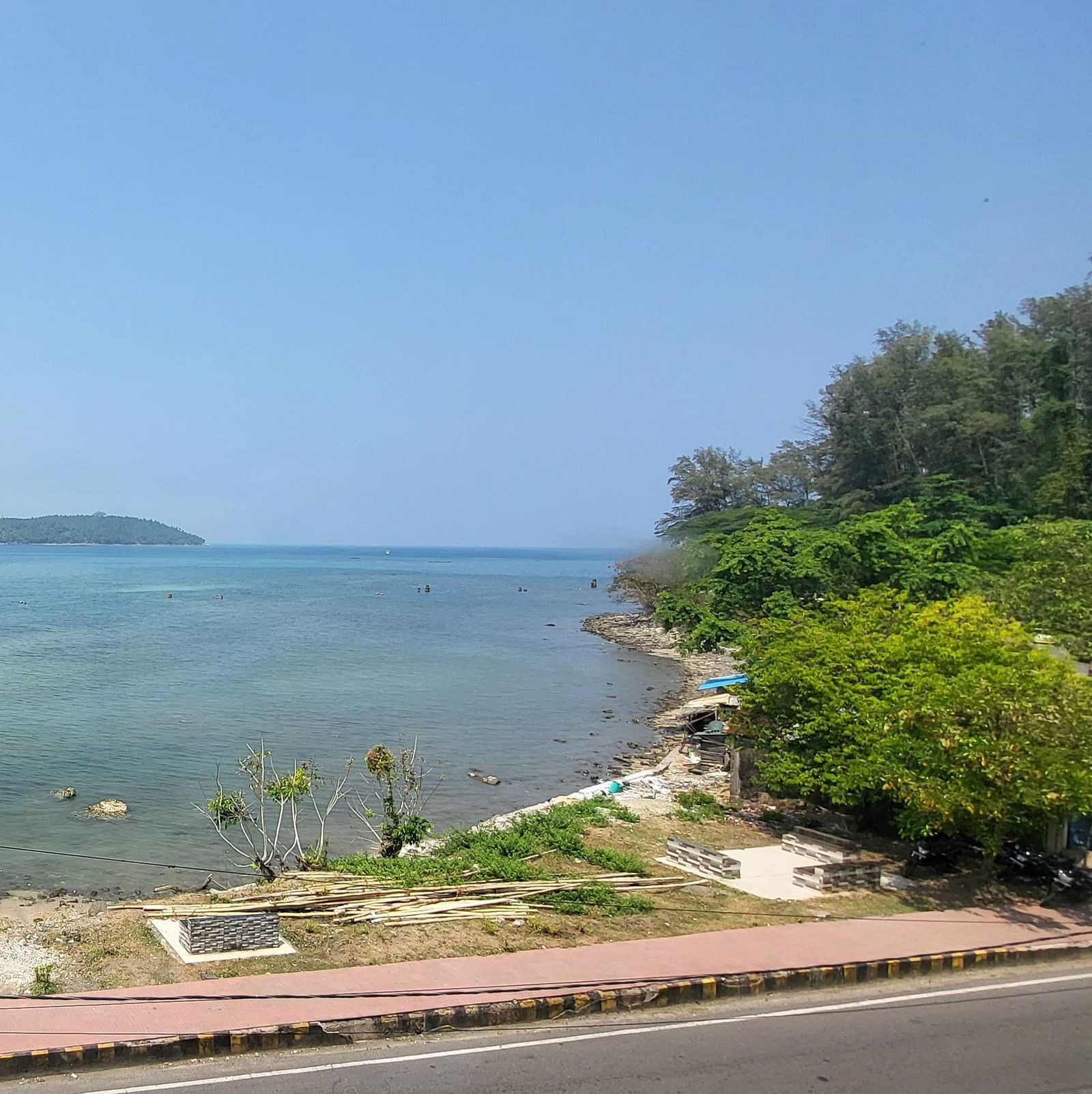 View of the ocean and the road outside 6ix Seashore Hotel, Port Blair along with trees on the shore