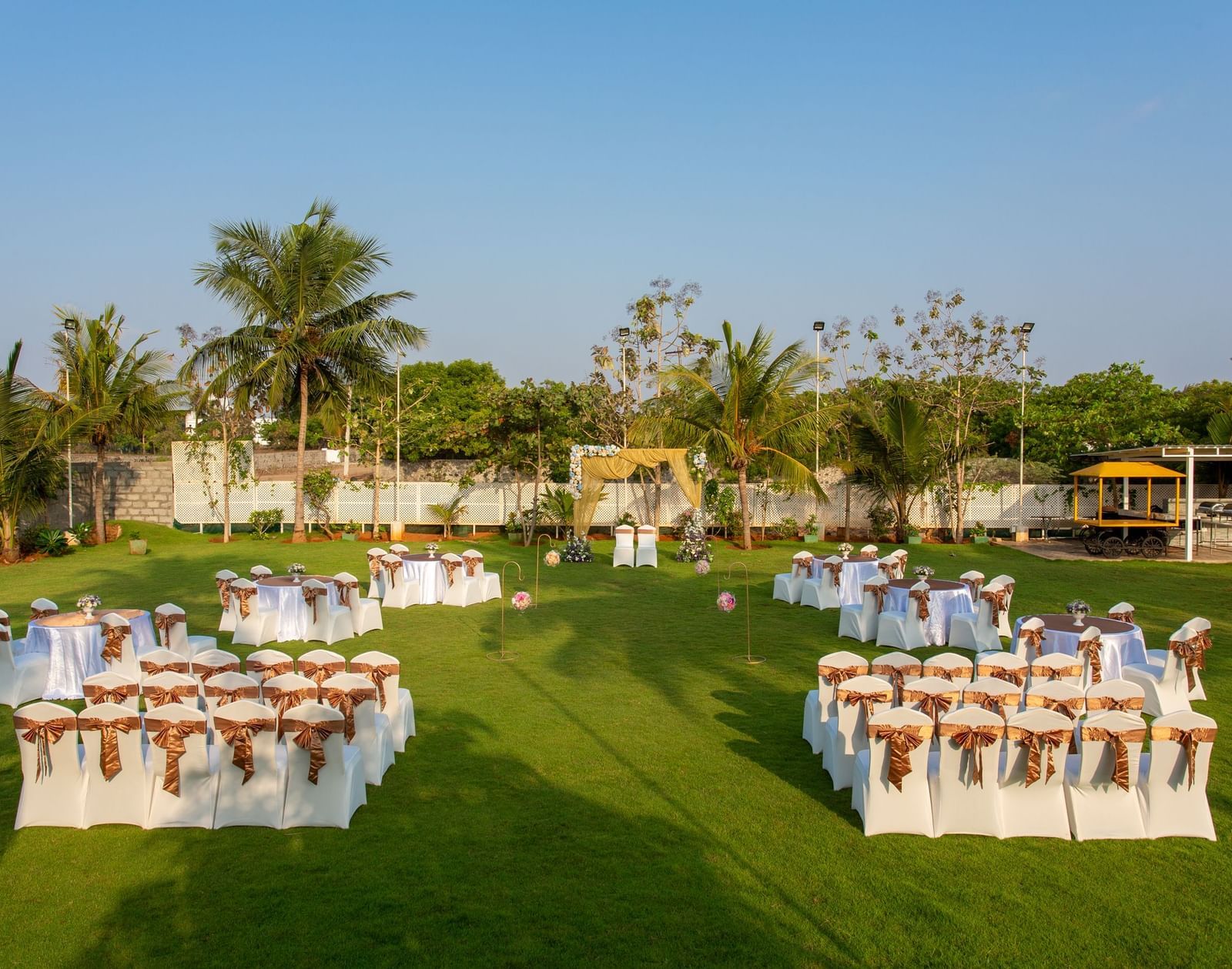 An outdoor event setup on a green lawn with neatly arranged tables and chairs, some covered in sashes, under a clear sky | Grande Pavillion | Grand Bay Resort and Spa