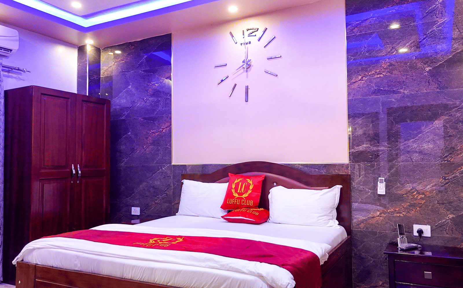 Hotel room interior with a bed, wall clock, wardrobe, and purple lighting - Luffu Club