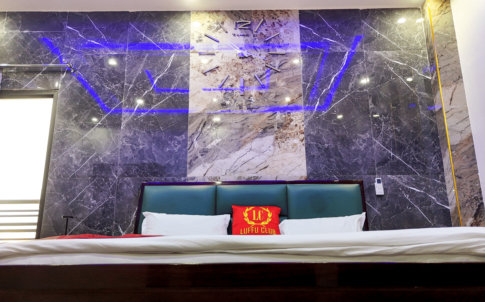 Close-up view of a hotel bed against a dark marble-style wall with blue accent lighting - Luffu Club