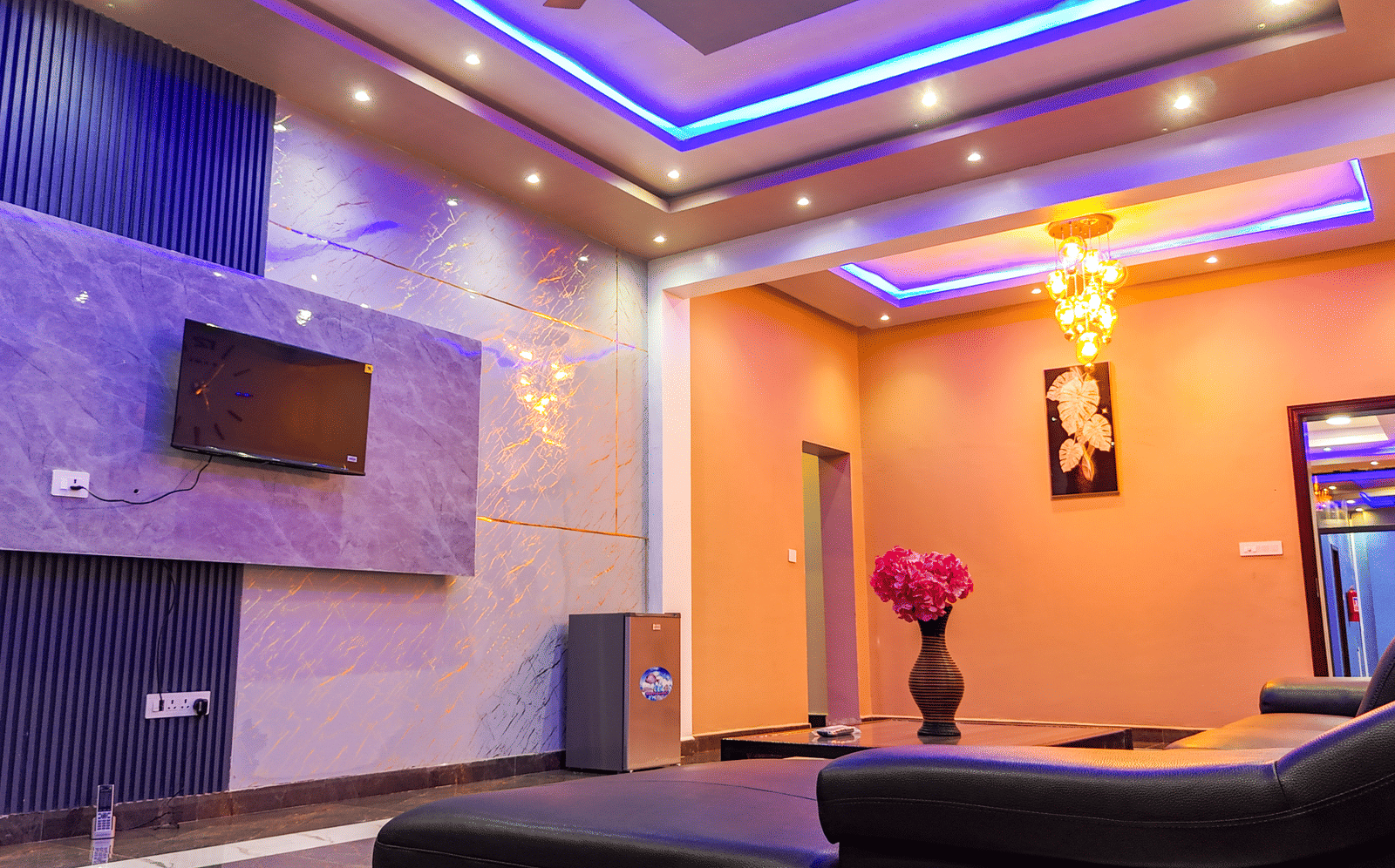 Living area with blue and purple accent lighting, a wall-mounted TV, and modern decor - Luffu Club
