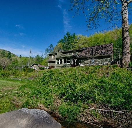 exterior image of the river house overlooking a lush green estate with a clear blue sky in the background - Historic Tapoco Lodge