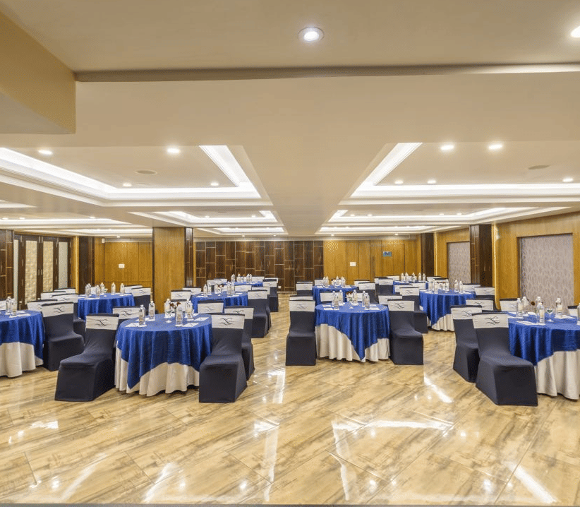 A well-lit conference room at The Citrine with blue and white tablecloths, chairs, and a stage setup.